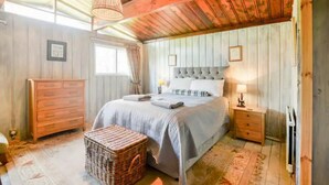 A cozy bedroom with a large bed, a wooden dresser, a wicker basket, and a ceiling fan. - Perfect wooden lodge for golfers & families, close to St. Andrews (New Gilston)