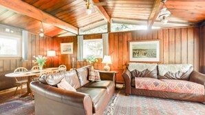 A cozy room with wooden walls and ceiling, a brown leather sofa, a matching armchair, a dining table with chairs, and a patterned rug. - Perfect wooden lodge for golfers & families, close to St. Andrews (New Gilston)