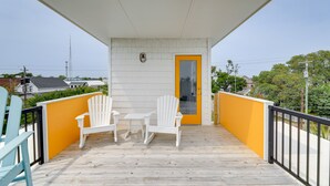Un balcon avec deux fauteuils Adirondack blancs et une petite table, une porte jaune et un mur extérieur blanc.