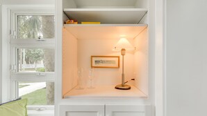 Un meuble blanc avec une étagère sur laquelle se trouvent un tableau encadré, une lampe et deux verres à vin.