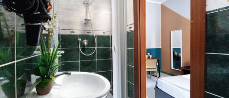 Un baño con un lavabo blanco, una ducha y una planta en maceta.