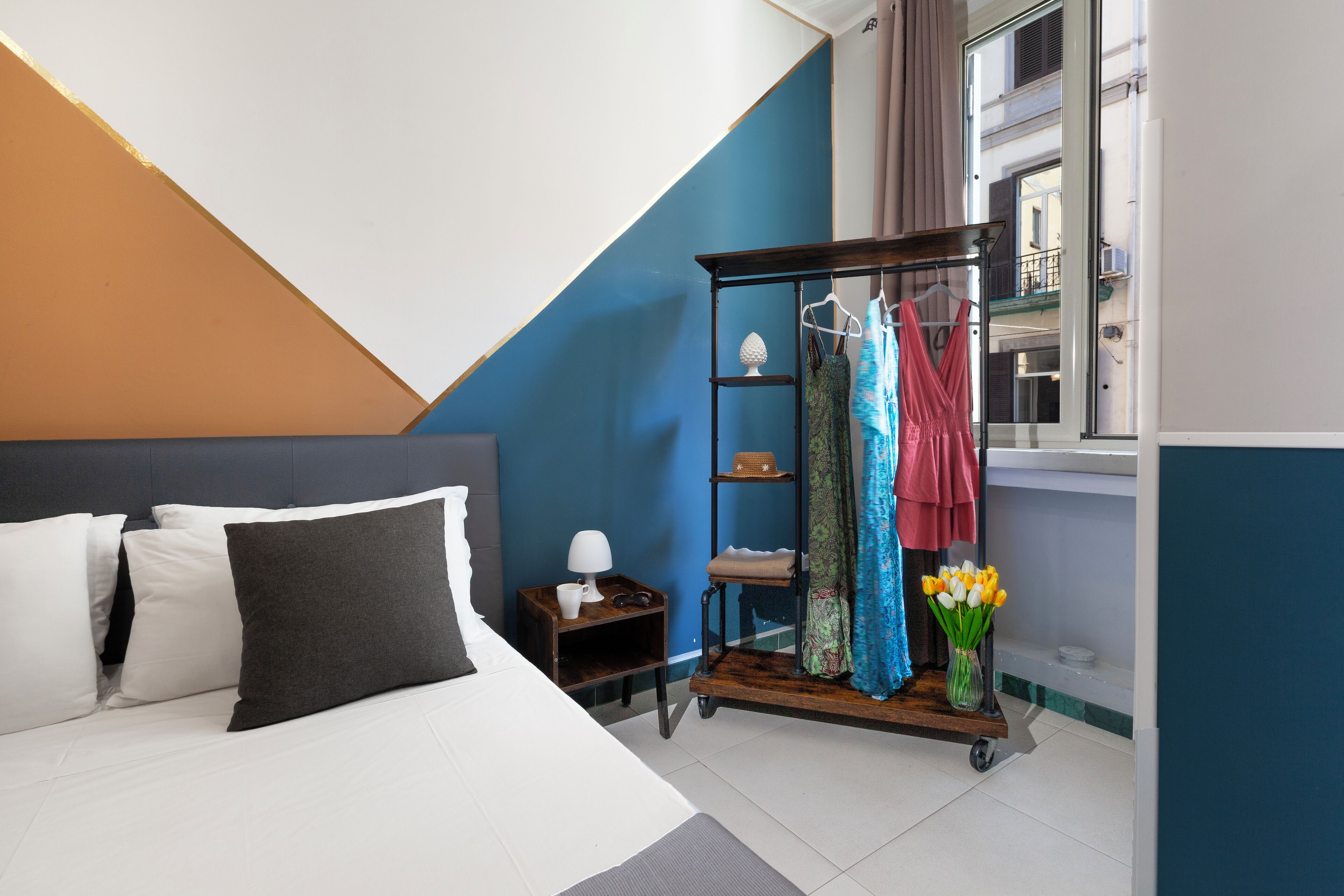 A modern hotel room with a bed, a nightstand, a wardrobe, and a window with curtains.
