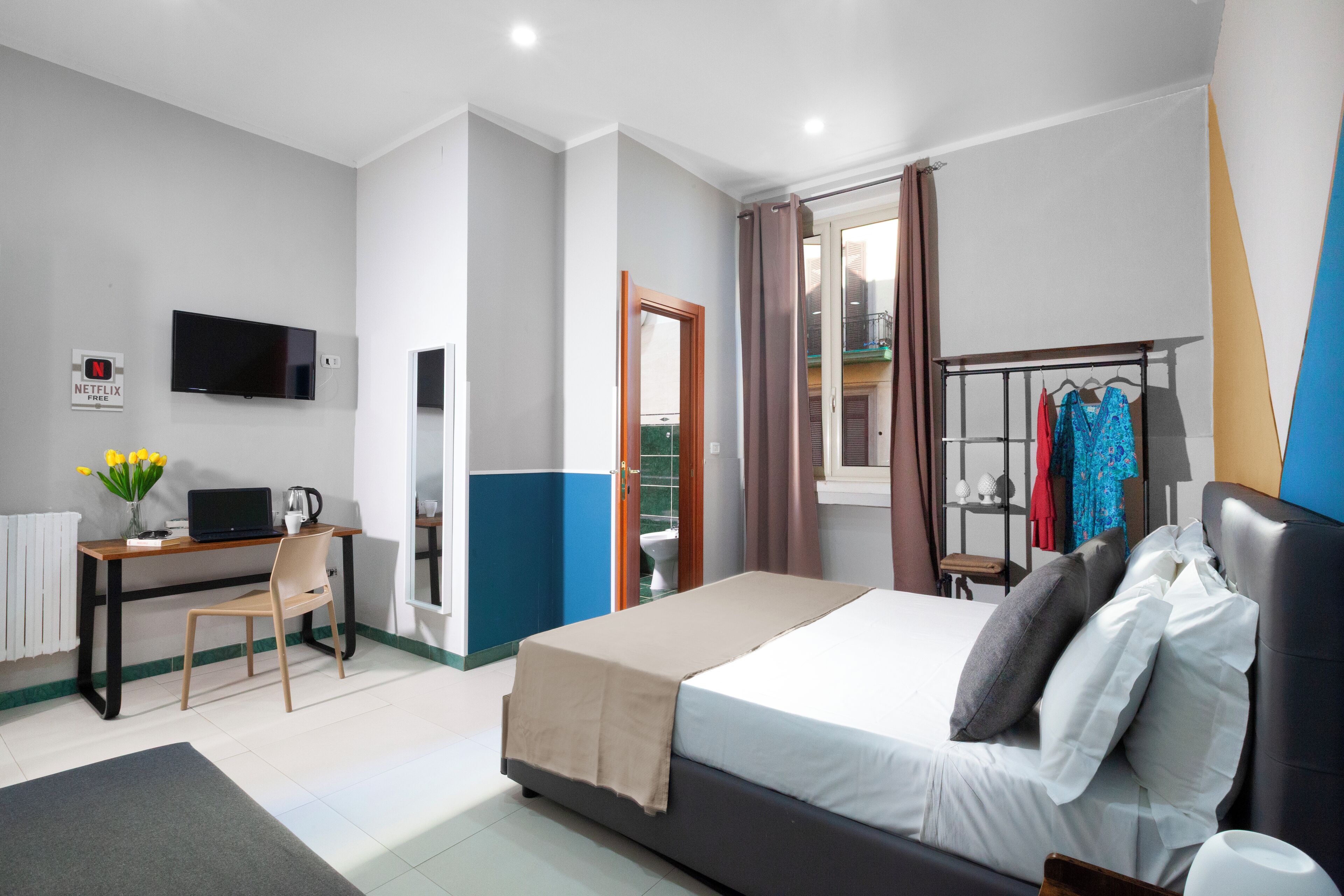 A hotel room with a bed, desk, chair, TV, and a view of the outside.