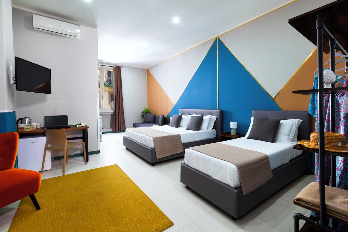 A hotel room with two beds, a desk, a chair, and a TV.