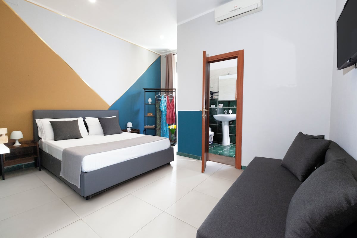 A bedroom with a bed, a nightstand, a dresser, a mirror, and a bathroom with a sink and toilet.