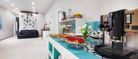 A modern kitchen with a coffee machine, a fruit display, and a seating area with a black sofa.