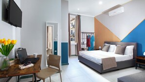 A bedroom with a bed, bedside table, and a desk with a laptop and a vase of flowers. - Royal Rooms Station Napoli (Naples)