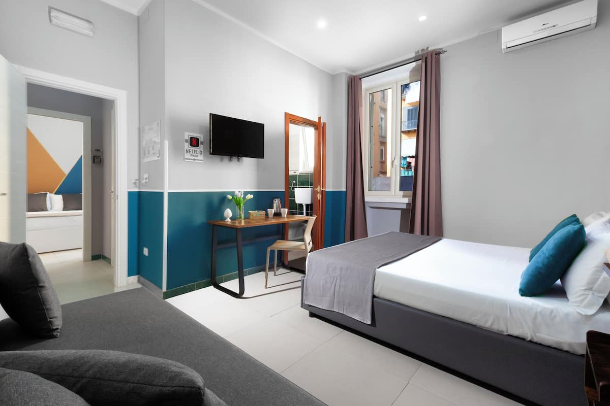 A modern hotel room with a bed, a desk, a chair, a TV, and a window with curtains.