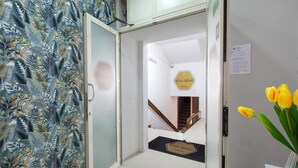 A hotel entrance with a tropical leaf-patterned wall, a staircase leading to the second floor, and a doormat with the hotel's name. - Royal Rooms Station Napoli (Naples)