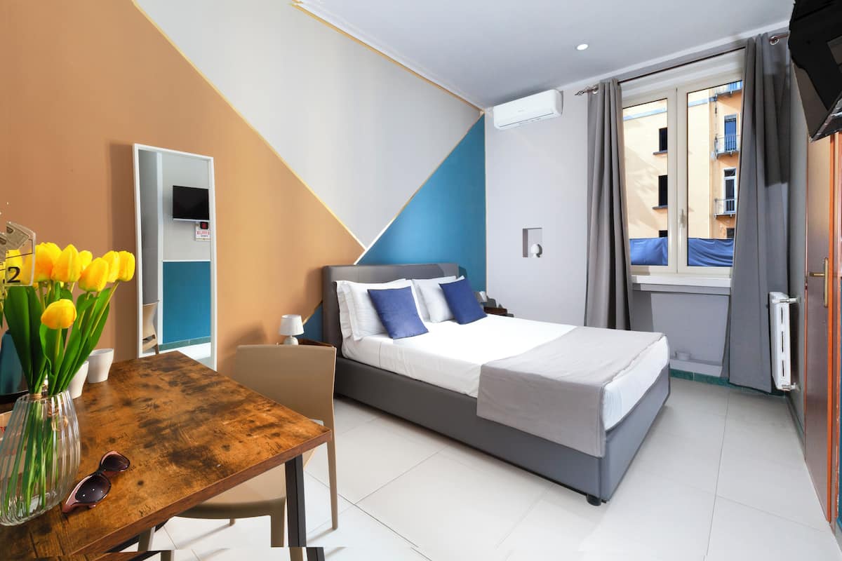 A modern hotel room with a bed, a desk with a vase of flowers, a chair, and a view of the outside balcony.