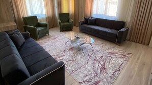 Ein geräumiges Wohnzimmer mit einem dunklen Sofa, einem grünen Sessel, einem grauen Sofa und einem Glastisch.