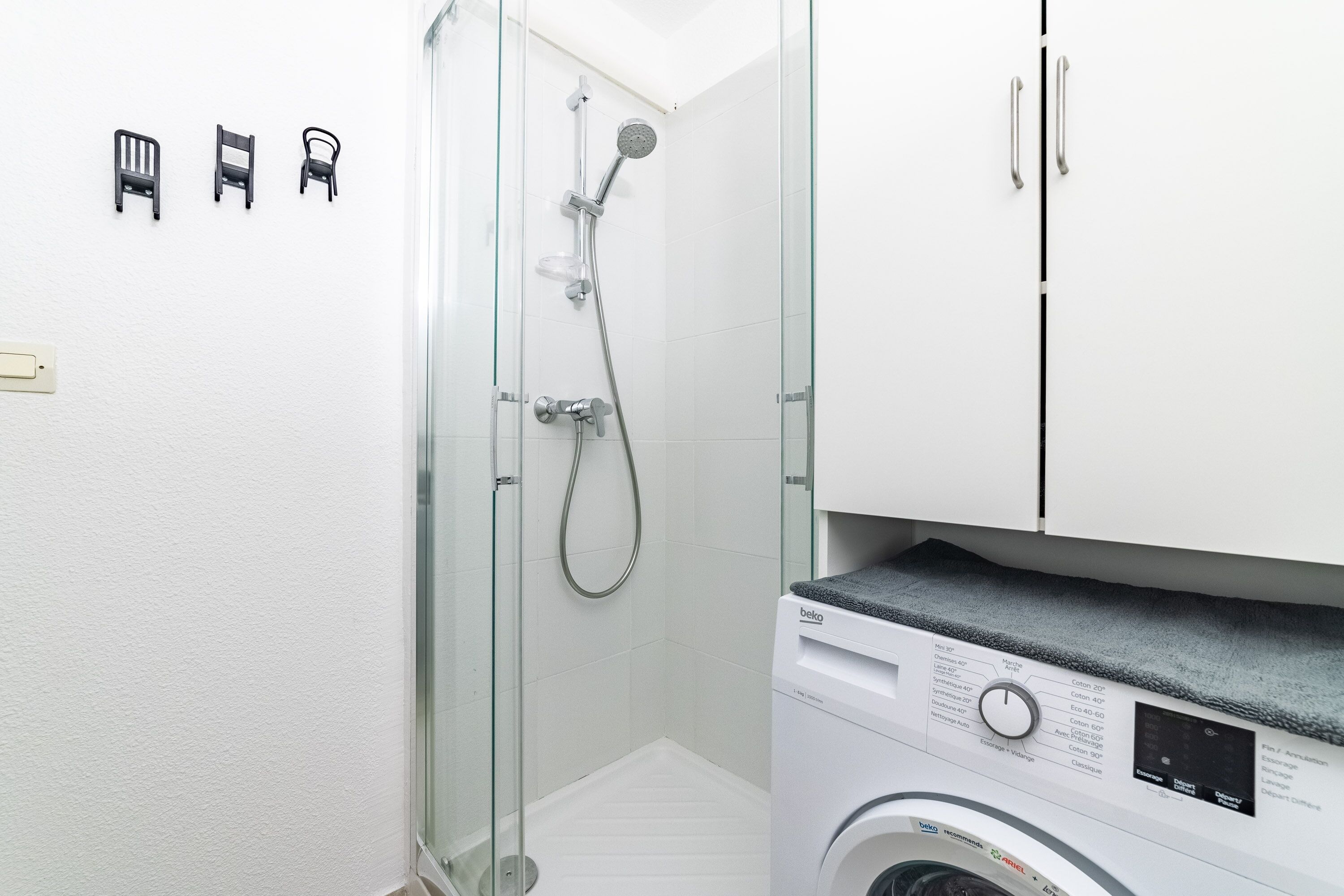 Une petite salle de bain dotée d’une douche à parois de verre, d’un lave-linge et d’un meuble avec un porte-serviettes.
