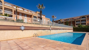 A swimming pool with a tiled deck, surrounded by a building with balconies and palm trees. - La Castillane - Appt avec piscine partagée (Cavalaire-sur-Mer)