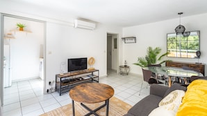 A modern living room with a TV, sofa, round coffee table, and dining area with a glass table. - La Castillane - Appt avec piscine partagée (Cavalaire-sur-Mer)