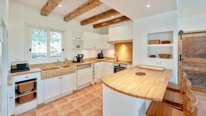 A modern kitchen with white cabinets, wooden beams, a large window, and a wooden island with seating. - Casa Hestia - Avec piscine privée (Entrecasteaux)