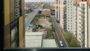 A view from a high-rise building overlooking a cityscape with modern architecture, a road, and some greenery.