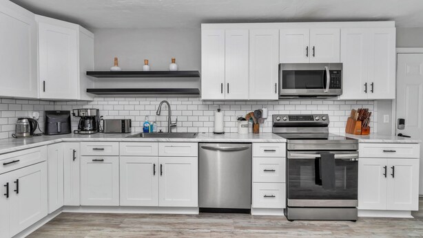 A modern kitchen with white cabinets, a stainless steel dishwasher, a microwave, a coffee maker, and an oven.