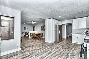 A modern kitchen with white cabinets, a stainless steel refrigerator, and a dining area with a table and chairs.