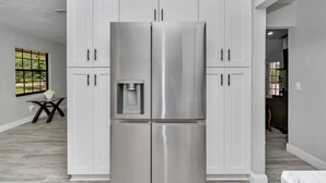 A modern kitchen with white cabinetry, a stainless steel refrigerator, and a built-in water dispenser.