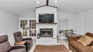 A modern living room with a fireplace, two sofas, a coffee table, and a TV mounted above the fireplace.