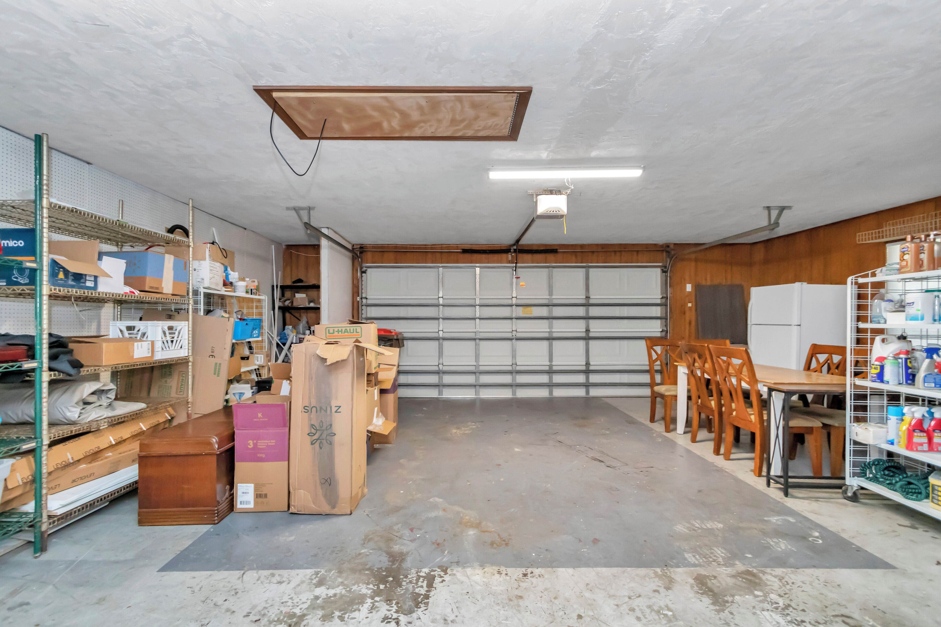 Un garage avec une table en bois, des chaises et des étagères remplies de boîtes et d’objets divers.