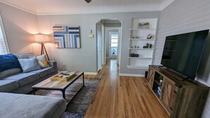 A modern living room with a grey sofa, wooden coffee table, and a TV on a wooden cabinet. - Downtown Royal Oak & Ferndale 3bd w/ King Master (Royal Oak)