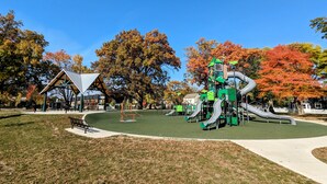 A playground with slides and climbing structures, surrounded by trees with autumn foliage. - Downtown Royal Oak & Ferndale 3bd w/ King Master (Royal Oak)