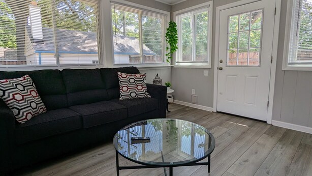 A room with a dark-colored sofa, a glass coffee table, and large windows with blinds. - Downtown Royal Oak & Ferndale 3bd w/ King Master (Royal Oak)