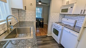 A modern kitchen with white cabinets, a granite countertop, a stainless steel sink, a microwave, a stove, and a ceiling fan. - Downtown Royal Oak & Ferndale 3bd w/ King Master (Royal Oak)