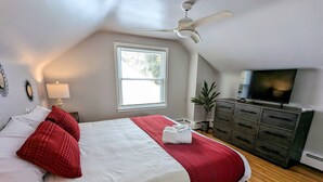 A bedroom with a bed, a TV, a ceiling fan, a window, and a plant. - Downtown Royal Oak & Ferndale 3bd w/ King Master (Royal Oak)
