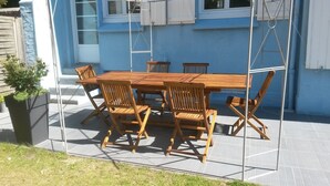An outdoor wooden table and chairs set on a patio with a blue building in the background.