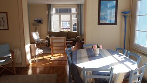 A dining area with a table set for four, surrounded by blue chairs, a white pitcher with flowers, and a blue floor lamp.