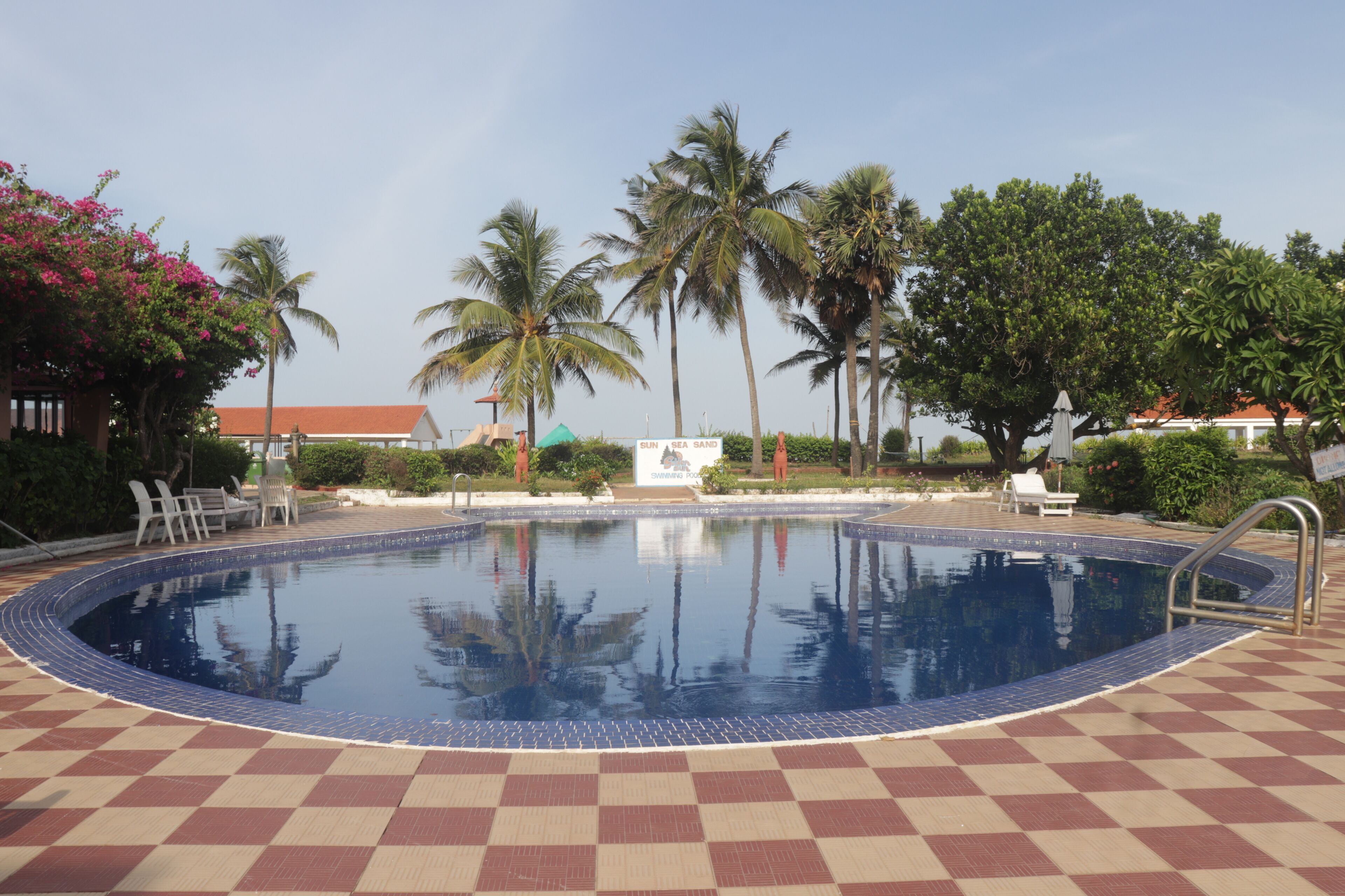 Ein Swimmingpool mit Schachbrettmuster, umgeben von Palmen und Liegestühlen.