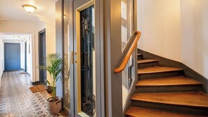 A hallway with a wooden staircase, a glass door, and a potted plant. - Charming 1820s Flat with Elevator & Queen size bed, near the Louvre (Paris)