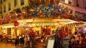 Un café al aire libre concurrido, con toldo a rayas y un letrero que dice "LE BON PECHEUR".