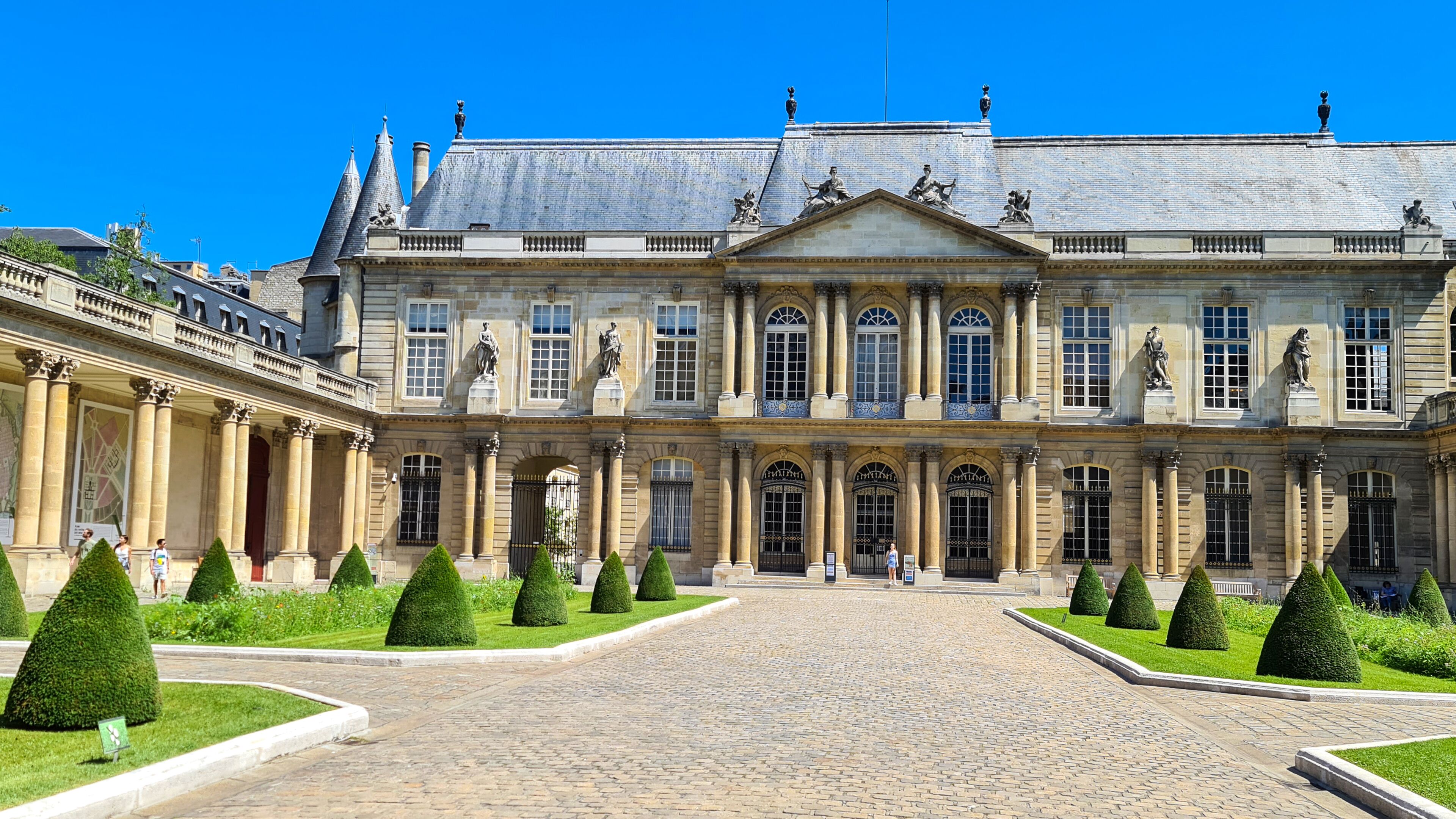 A grand historic building with a symmetrical facade, large windows, and statues.