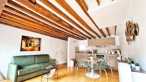 A modern living room with a green sofa, a glass coffee table, and a dining area with a glass table and chairs. - Charming 1820s Flat with Elevator & Queen size bed, near the Louvre (Paris)