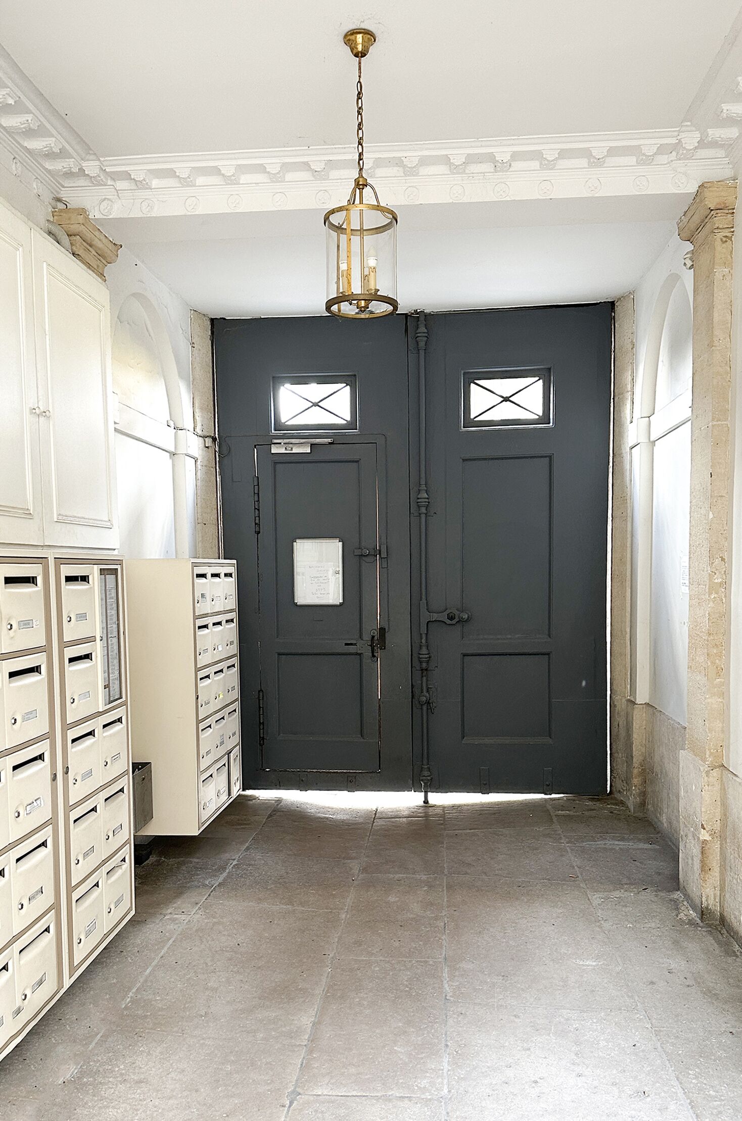 Un pasillo con una puerta gris oscuro, una lámpara y varios archivadores beige.