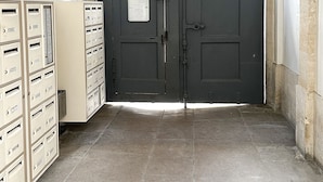 A hallway with a dark grey door, a light fixture, and a set of beige filing cabinets. - Charming 1820s Flat with Elevator & Queen size bed, near the Louvre (Paris)