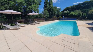 A rectangular swimming pool with a curved edge, surrounded by a tiled deck. There are lounge chairs and umbrellas along the poolside. - Studio "nid Cosy" Avec Piscine Chauffée (Bonnemain)