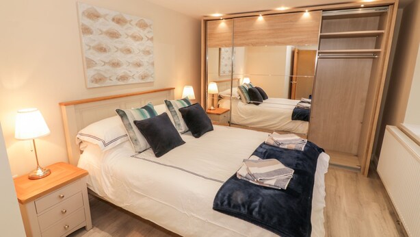 A neatly arranged bedroom with a bed, bedside tables, a mirror, and a wardrobe. - Bay View (Criccieth)