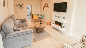 A modern living room with a grey sofa, a coffee table, a TV mounted on the wall, and a fireplace with decorative items. - Bay View (Criccieth)