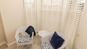 Two wicker chairs with patterned cushions and a small table, positioned in front of a window with white blinds. - Bay View (Criccieth)