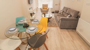 A modern living room with a dining area, featuring a sofa, a glass table with plates, and a television mounted on the wall. - Bay View (Criccieth)