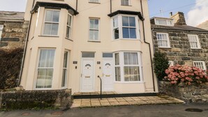 A two-story building with bay windows, a stone facade, and a small garden with pink flowers. - Bay View (Criccieth)