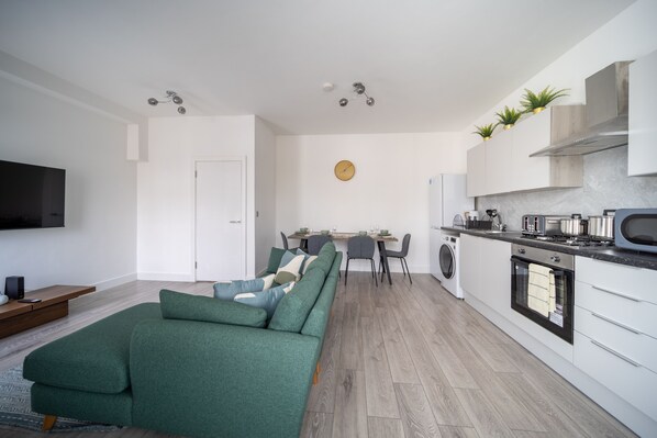 A modern living room with a green sofa, a flat-screen TV, and a dining area with a table and chairs.