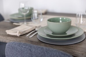 A dining table with a green bowl and plates, a folded napkin, and a glass.