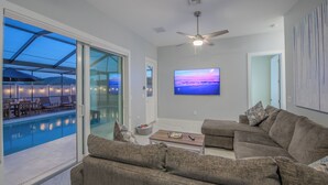 Un salon moderne avec vue sur la piscine, un ventilateur de plafond et un grand téléviseur mural.