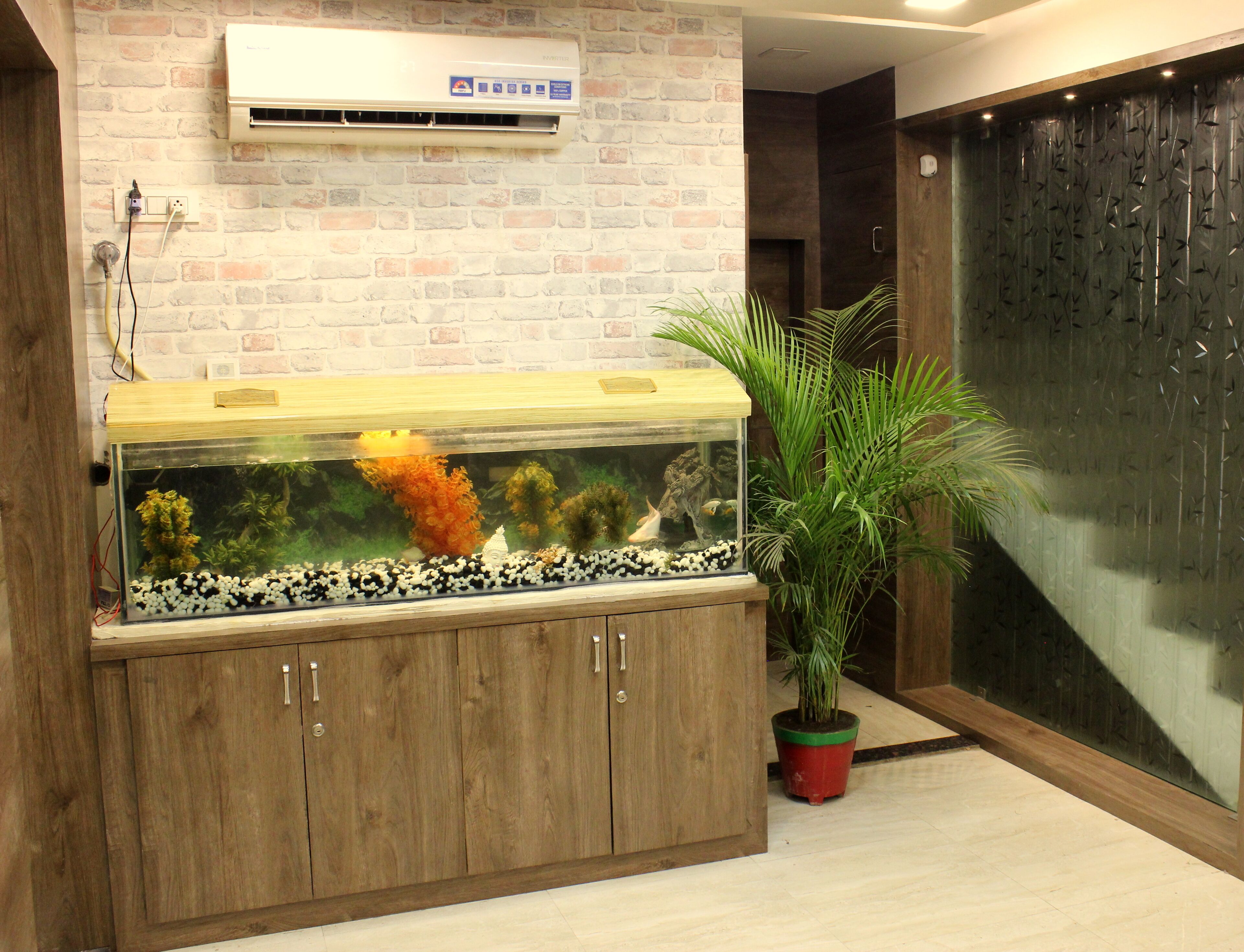 Un acuario con plantas acuáticas y adornos, un aparador de madera debajo, y una planta en maceta a su lado.