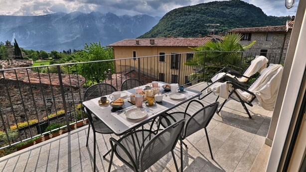 A balcony with a table set for breakfast, overlooking a mountainous landscape. - Appartamento Lucia by Theater Home - with big balcony and a panoramic view (Tignale)